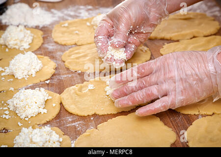 Eine Nahaufnahme eines weiblichen Baker in Schutzhandschuhe zieht den Teig für das Kochen von Brötchen mit Käse auf einer verknoteten Tabelle mit einem Nudelholz Stockfoto