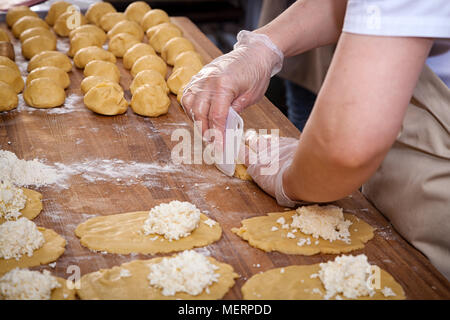 Eine Nahaufnahme eines weiblichen Baker in Schutzhandschuhe zieht den Teig für das Kochen von Brötchen mit Käse auf einer verknoteten Tabelle mit einem Nudelholz Stockfoto