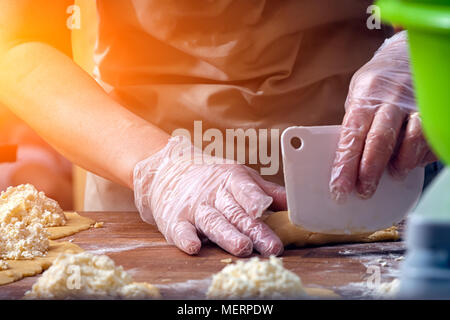 Eine Nahaufnahme von einem Bäcker in einem armen Schürze formt einen Hot dog Brötchen an einem hölzernen Tisch in einer Bäckerei Stockfoto