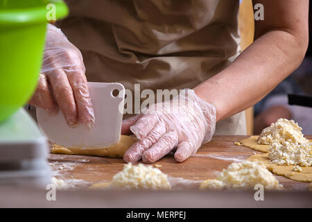 Eine Nahaufnahme von einem Bäcker in einem armen Schürze formt einen Hot dog Brötchen an einem hölzernen Tisch in einer Bäckerei Stockfoto