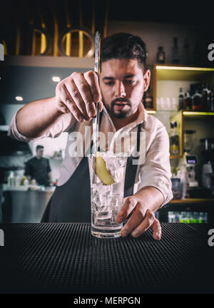 Barkeeper in einem weißen Hemd und schwarze Schürze, Hinzufügen einer Scheibe Ingwer in ein Glas Stockfoto