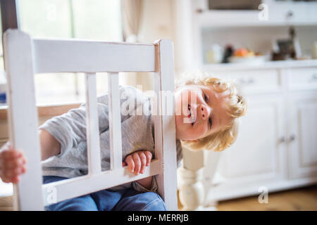 Ein Kleinkind Junge auf dem Stuhl, zu Hause zu sitzen. Stockfoto