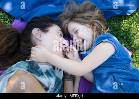 Frau Mutter und vier Jahre alt blond Kind zusammen lachen liegen auf Handtücher in das grüne Gras der Park Stockfoto