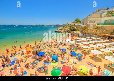 Cascais, Portugal - August 6, 2017: die Menschen beim Sonnenbaden auf Praia da Rainha, ein kleiner Strand mit Felsen im Zentrum von Cascais, Lissabon Küste. Türkisblaues Meer in den Sommerferien. Fischereihafen für den Hintergrund. Stockfoto