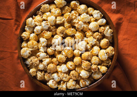 Hölzerne Schüssel mit süßem Popcorn auf orange Bettwäsche. Snacks und Essen für einen Film. Ansicht von oben mit der Kopie. Stockfoto