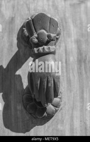 Isoliert, Nahaufnahme von einem reich verzierten alten Metall Türklopfer in Form einer Hand, montiert auf eine körnige Holztür, mit einem Schatten, in Schwarz und Weiß Stockfoto