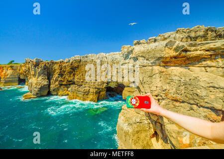 Hell's Mouth, Atlantische Küste von Cascais, Portugal. Mobiltelefon mit Portugal Flagge Abdeckung Fotos von Boca do Inferno eine natürliche Arch in rauen Klippe Bildung. Tourismus und Reisen Konzept in Portugal Stockfoto