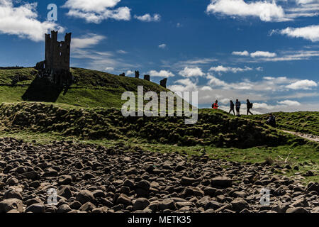 Wanderer auf der Northumberland Küste Weg vorbei an den Ruinen von Dunstanburgh Castle. In der Nähe Craster, Northumberland, Großbritannien. April 2018. Stockfoto