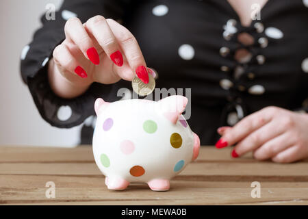 Weibliche Hand, die eine Euro Münze über piggy Bank als Konzept Bild zum Speichern oder für Investitionen Stockfoto