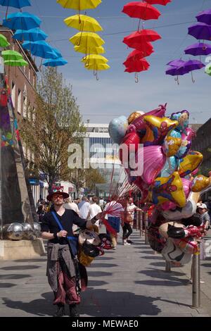 Ballon Verkäufer auf Exeter High Street mit der Exeter Rätsel Obelisk Skulptur und farbenfrohen Frühling Sonnenschirme. Devon, UK. April, 2018. Stockfoto