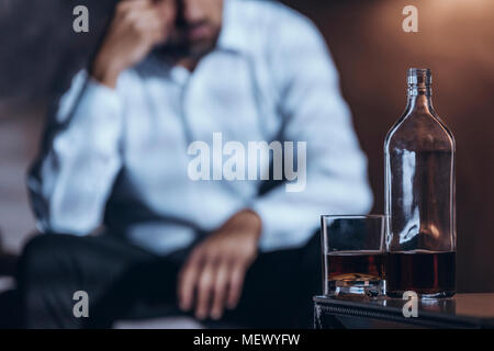 Whiskey Flasche und Glas mit einer depressiven Mann im Hintergrund Stockfoto