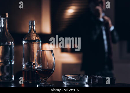 Flasche, Glas mit Alkohol und Zigaretten mit einem Geschäftsmann im Hintergrund Stockfoto