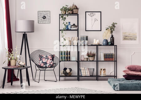 Kissen mit Blumenmuster auf Sessel neben Silber Lampe im Wohnzimmer Interieur mit Plakat und Blumen Stockfoto