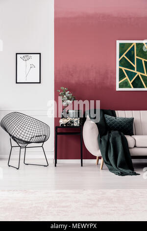 Grüne Decke auf dem Sofa gegen rote Wand mit Malerei in Wohnzimmer Einrichtung mit Sessel Stockfoto