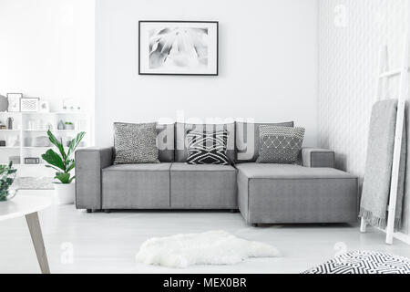 Graue Ecke Couch mit drei gemusterten Kissen im hellen Wohnzimmer Interieur mit Malerei und weissen Teppich stehend Stockfoto