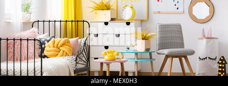 Gelbe Knoten Kissen auf Metall Bett im Schlafzimmer Innenraum pastell Kind mit grau Stuhl Stockfoto