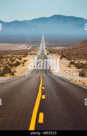 Klassische vertikale Ansicht von einem endlosen geraden Straße durch die karge Landschaft der berühmten Death Valley mit extremer Hitze Dunst im Sommer Stockfoto