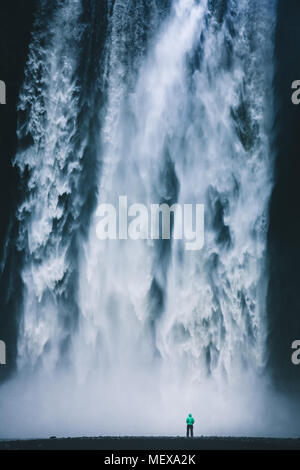 Vertikale Panorama der Wanderer in farbenfrohen Regenjacke stand vor der gigantischen Wasserfall Skogafoss, Skogar, Island Stockfoto