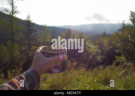Punkt einer Ansicht, mans hand eine Tasse Kaffee im Freien auf einer Wanderung, mit Blick auf eine Berglandschaft Stockfoto