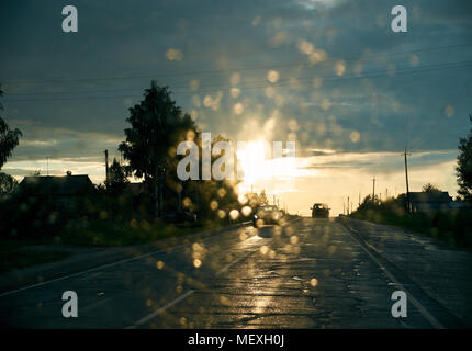 Blick aus dem Autofenster auf dem nassen County Road Ahead bei Sonnenuntergang, bokeh Kreise Stockfoto