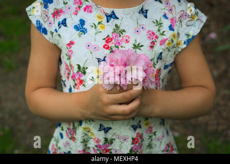 Mädchen im Blümchenkleid Holding einen kleinen Blumenstrauß aus rosa Blüten Stockfoto