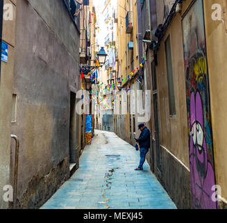 Ein Mann lehnt sich gegen eine Wand in einer engen Straße im Gotischen Viertel von Barcelona sein Mobiltelefon zu überprüfen, Stockfoto