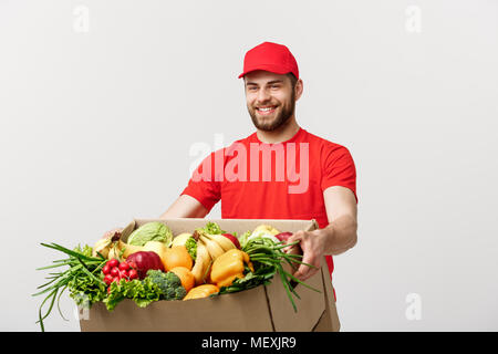 Lieferung Konzept: Stattlichen kaukasischen Lebensmittel-lieferservice Kurier Mann in der roten Uniform mit Lebensmittelgeschäft, mit frischem Obst und Gemüse Stockfoto