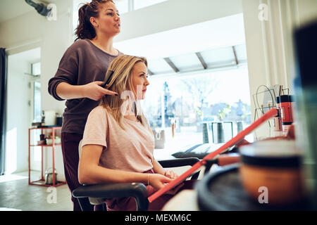 Blonde junge Frau sitzt in einem Salon Stuhl durch Haarfärbemittel Proben mit ihr Hairstylist Stockfoto