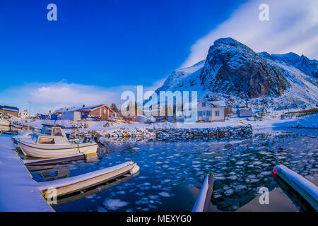 Leknes, LOFOTEN, Norwegen - 10 April, 2018: Im freien Blick auf Fischerboot im Hafen mit einigen Gebäude hinter und riesigen Berg mit Schnee in Leknes, Lofoten County abgedeckt Stockfoto