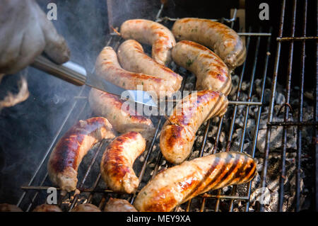 Frische Wurst. Heiße Hunde Grillen im Freien auf ein Gas Grill. Männliche flips gegrillte Würstchen Kochen auf offenem Feuer. Stockfoto