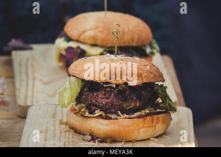 Zwei Handwerk Rindfleisch Burger auf Holztisch auf schwarzem Hintergrund isoliert. Der Prozess, in dem Burger Stockfoto