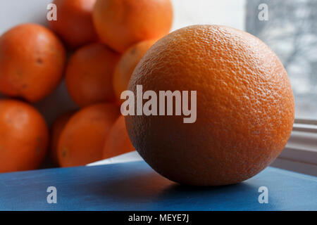 Orange auf der blauen Fläche vor der unscharfen Obst Hintergrund. Fensterbänke Stockfoto
