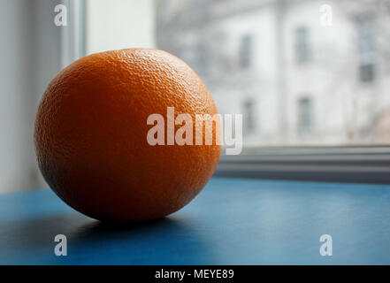 Seitenansicht einer orange Frucht auf eine blaue Fläche, die von der Sonne Licht vom Fenster beleuchtet Stockfoto
