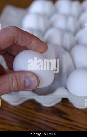 Ein Ei unter einer Gruppe von Eiern, die von einer Hand abgeholt werden Stockfoto