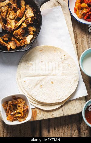 Chicken Fajitas. Mariniertes Huhn Stücke mit roten und gelben Paprika und Zwiebeln mit Tomate Salsa, Sour Cream und Tortilla Wraps Stockfoto