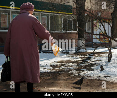 Alte einsame Frau im Winter Mantel Fütterung Vögel im Park. Zentrum der großen Stadt. Stockfoto