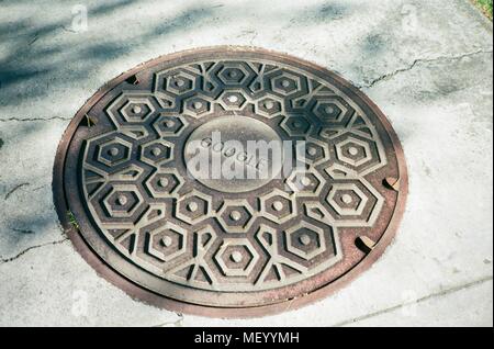 Google Logo warf in einem Mannloch utility Abdeckung, möglicherweise eine Komponente des Google LWL LWL-Netzwerk, an den Googleplex, das Silicon Valley Hauptsitz der Suchmaschine und Technologie Unternehmen Google Inc., Mountain View, Kalifornien, 14. April 2018. () Stockfoto