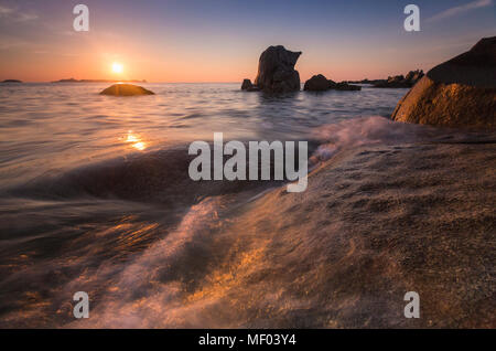 Wellen, die auf Felsen unter der feurigen Himmel bei Sonnenaufgang Punta Molentis Villasimius Cagliari Sardinien Italien Europa Stockfoto