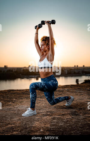 Junge fitness Frau tun Training mit Hanteln durch den Fluss in einem Sonnenuntergang. Stockfoto