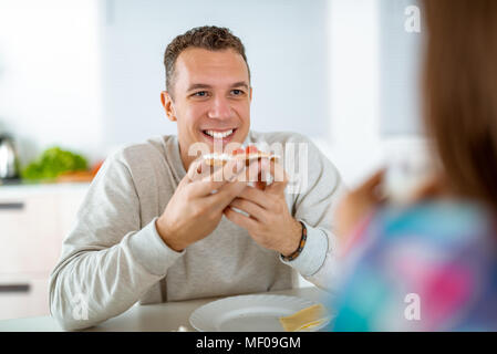 Porträt von einem gutaussehenden jungen Mann, der ist gesund essen Sandwich für das Frühstück in der heimischen Küche. Stockfoto