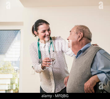 Älterer Mann an Krankenschwester holding Glas Wasser zu Hause lächeln Stockfoto