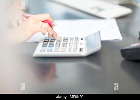 Frau am Schreibtisch im Büro mit Taschenrechner Stockfoto