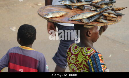 Afrikanischer Mann in traditioneller Kleidung gepolsterte ein Tablett mit getrockneten Fisch auf dem Kopf, Nahaufnahme, Elmina, Ghana Stockfoto