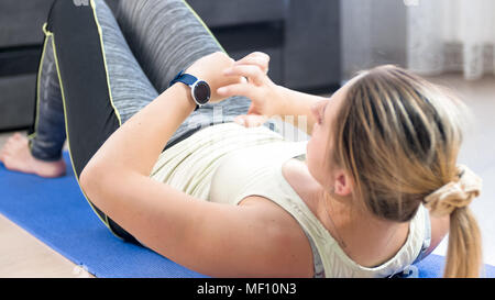 Junge Frau liegend auf Fitness Matte und mit Fitness smart Uhren Stockfoto