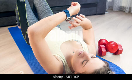 Junge Frau ihre Parameter auf Fitness smart Watch nach dem Training an Fitness Matte zu Hause Stockfoto