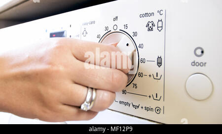 Nahaufnahme der weiblichen Hand drehen Temperatur Steuerung der Knopf auf Waschmaschine Stockfoto