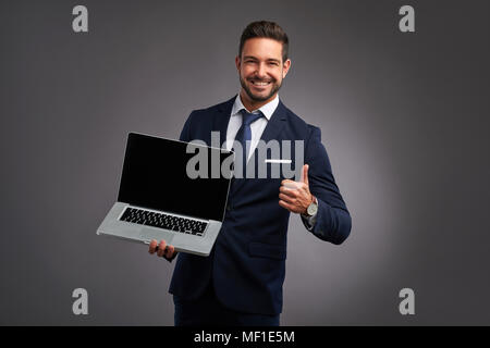 Eine elegante hübscher junger Mann, und zeigen Sie den Bildschirm eines Laptop während Daumen nach oben zeigt Stockfoto