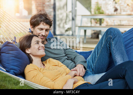 Lächelndes Paar in der Hängematte im Garten ihres Hauses liegen Stockfoto