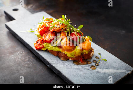 Crostini mit Garnelen und Tomaten, geröstete Brot, Kräuter, Avocadocreme, Sweet Chili Sauce, Jalapenos, Kresse Stockfoto