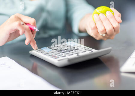 Frau am Schreibtisch im Büro mit Taschenrechner und Stress Ball Stockfoto